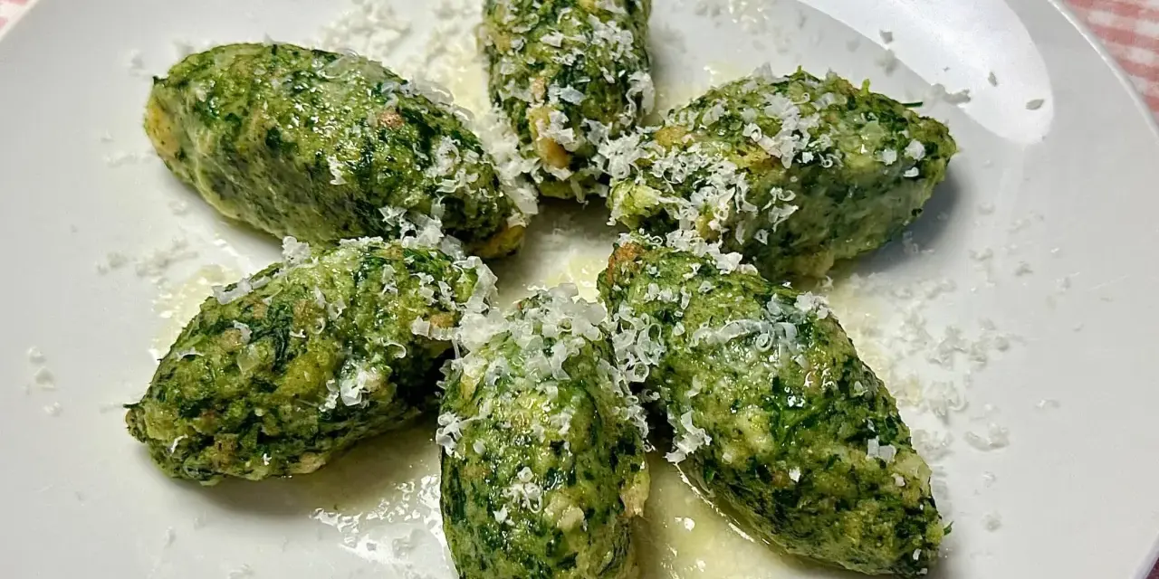 Strangolapreti alla trentina, verdi e saporiti, spolverati di formaggio grattugiato su un piatto bianco.