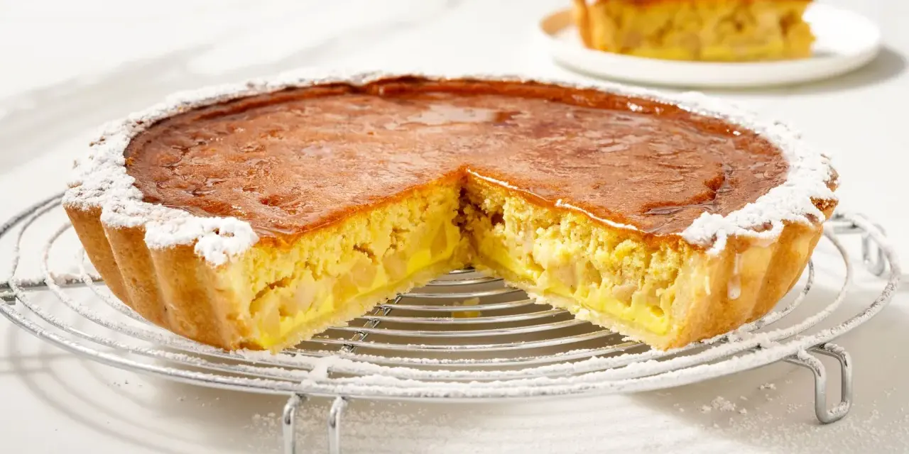 Una fetta di torta di mele con crema pasticcera, cosparsa di zucchero a velo, su una griglia.