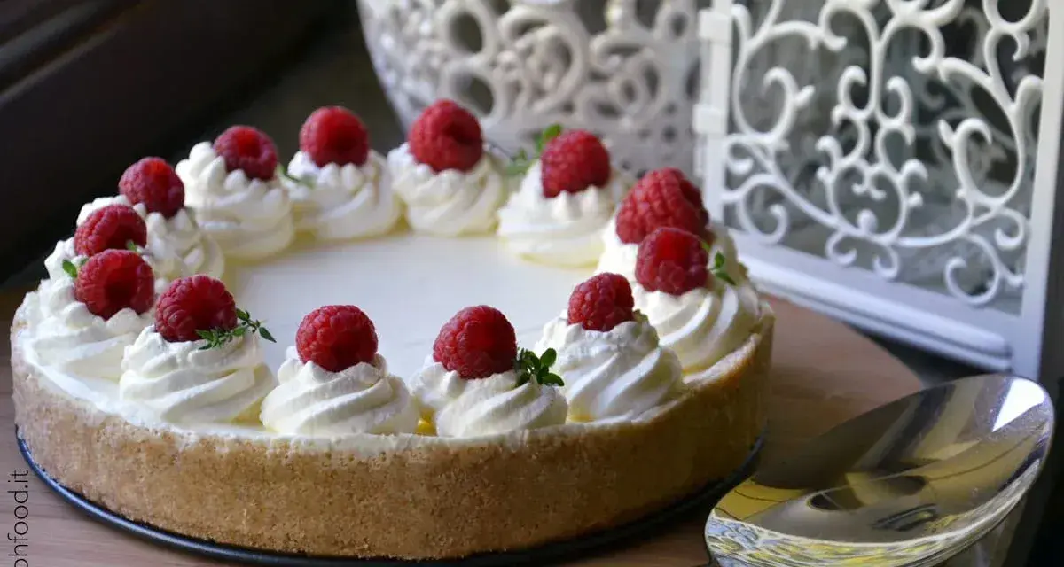 Cheesecake senza gelatina decorata con panna montata e lamponi freschi, pronta per essere servita.