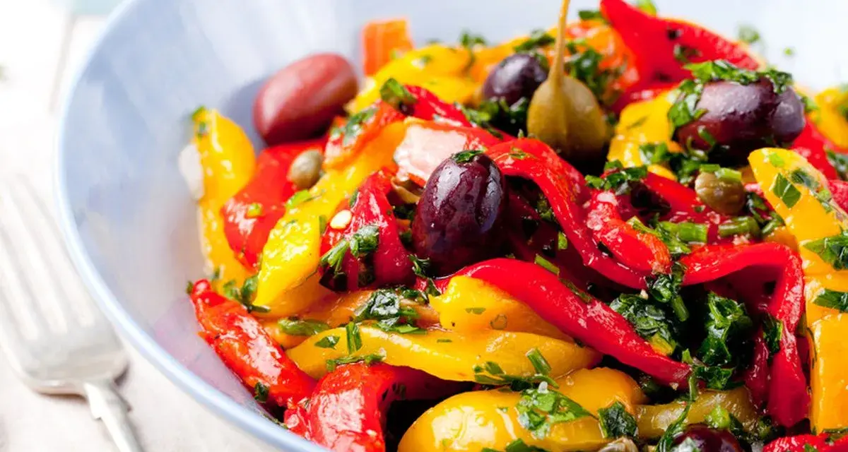 Peperonata ricetta della nonna: un piatto colorato con peperoni rossi e gialli, olive, capperi e prezzemolo fresco.