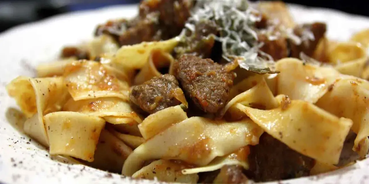Pappardelle al cinghiale fumanti, con pezzi di carne succulenta e una spolverata di parmigiano.