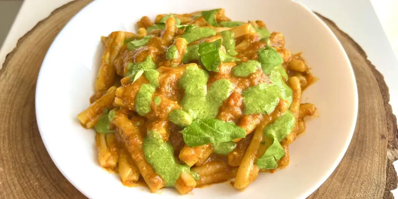 Un piatto di pasta alla Portofino, con un sugo rosso e un pesto verde brillante, guarnito con foglie di basilico fresco.