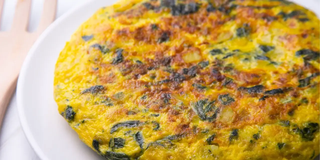 Frittata di spinaci dorata e invitante su un piatto bianco, con un utensile in legno sullo sfondo.