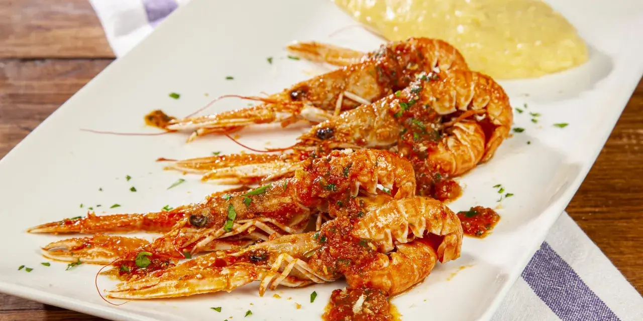 Scampi alla busara succulenti su piatto bianco, con un contorno di polenta gialla.