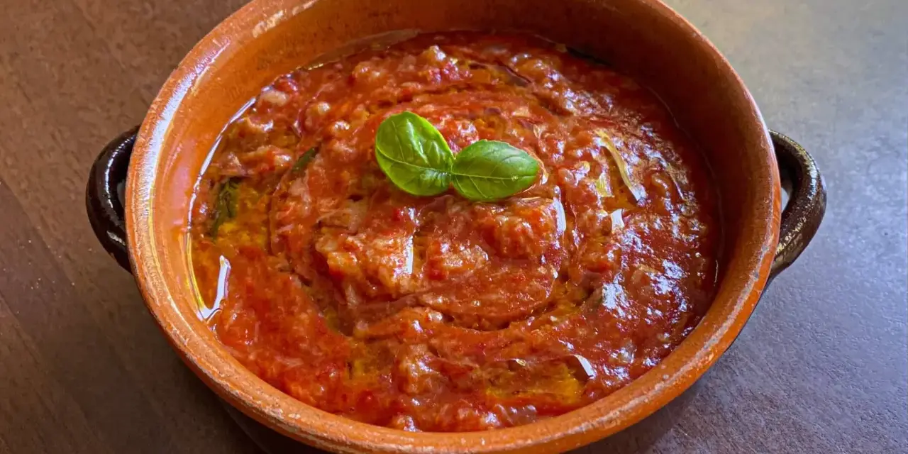 Piatto di pappa al pomodoro in terracotta, guarnito con basilico fresco. Un classico della cucina toscana.