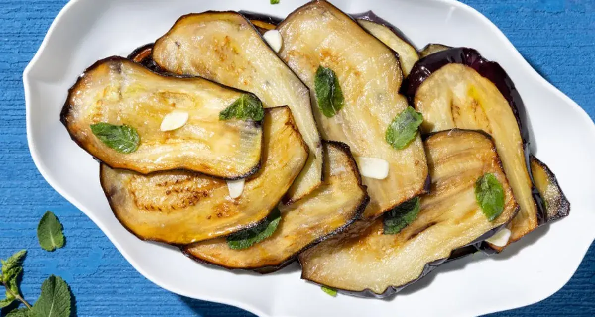 Fette di melanzane grigliate, guarnite con menta fresca e aglio, un contorno di verdure saporito.