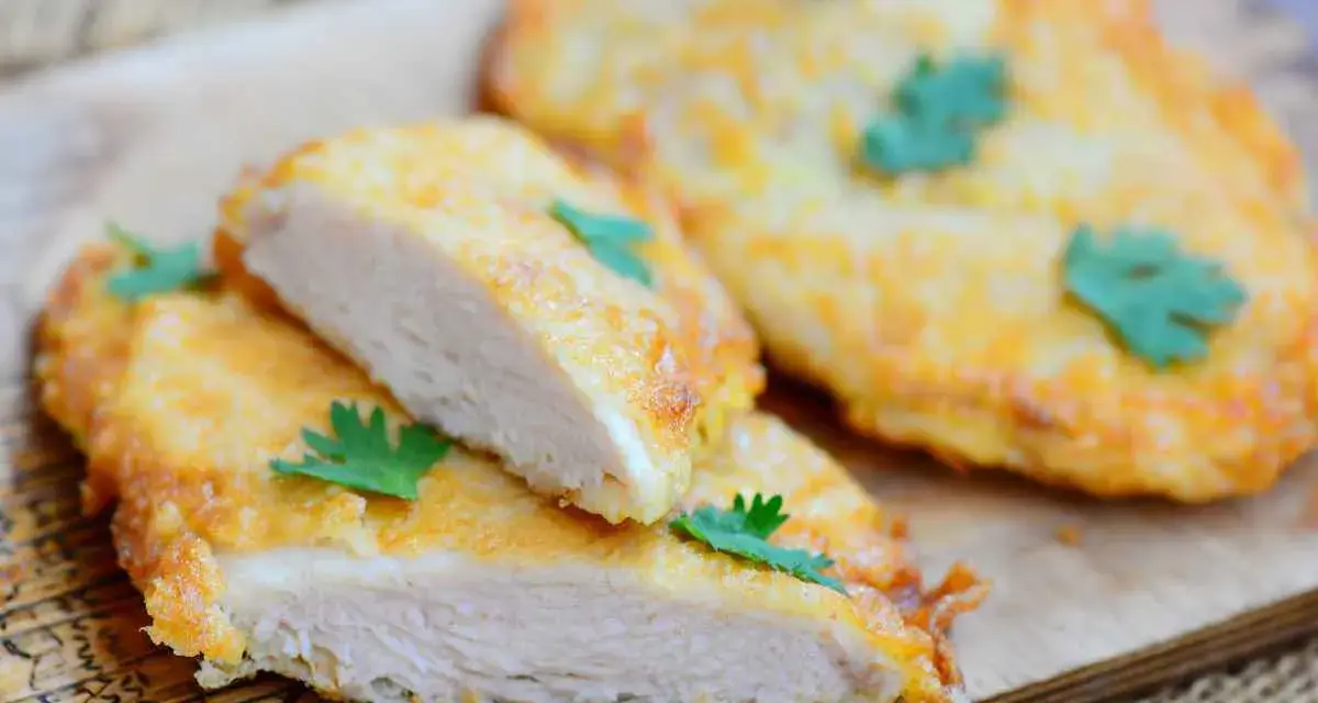 Deliziose cotolette di pollo dorate, tagliate a metà per mostrare la succosa carne bianca, guarnite con prezzemolo fresco.