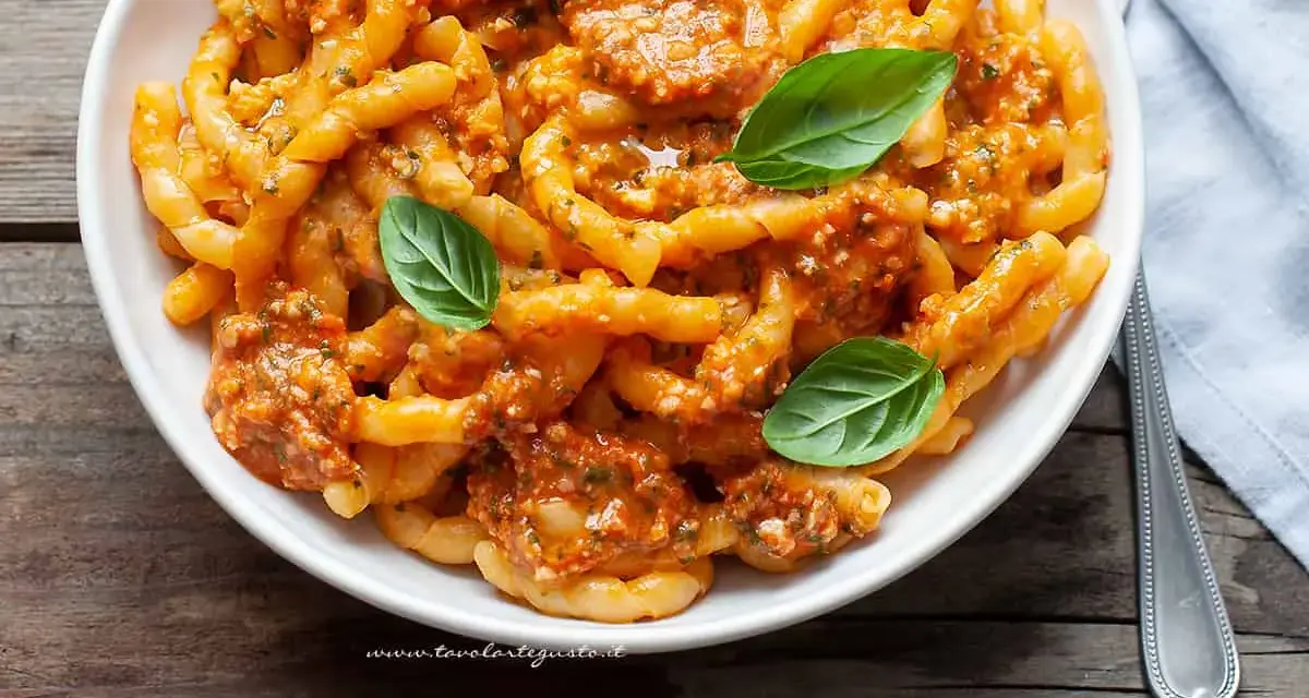 Busiate alla trapanese, un piatto di pasta siciliana con un ricco sugo rosso, guarnito con basilico fresco.