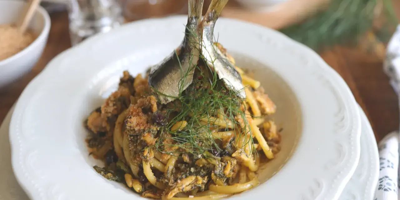 Un piatto di pasta con le sarde, guarnito con finocchietto fresco e due pesciolini interi. Un classico siciliano pronto da gustare.