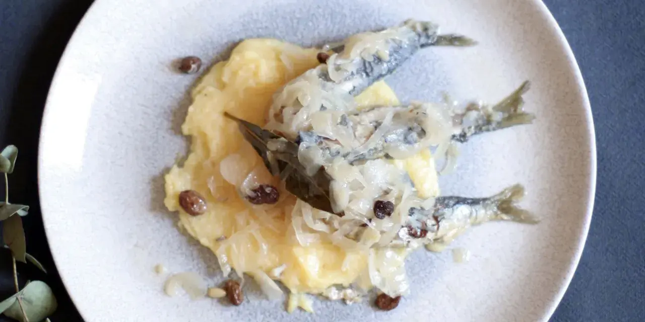 Sarde in saor su un letto di polenta, con cipolle caramellate e uvetta. Un classico veneto.