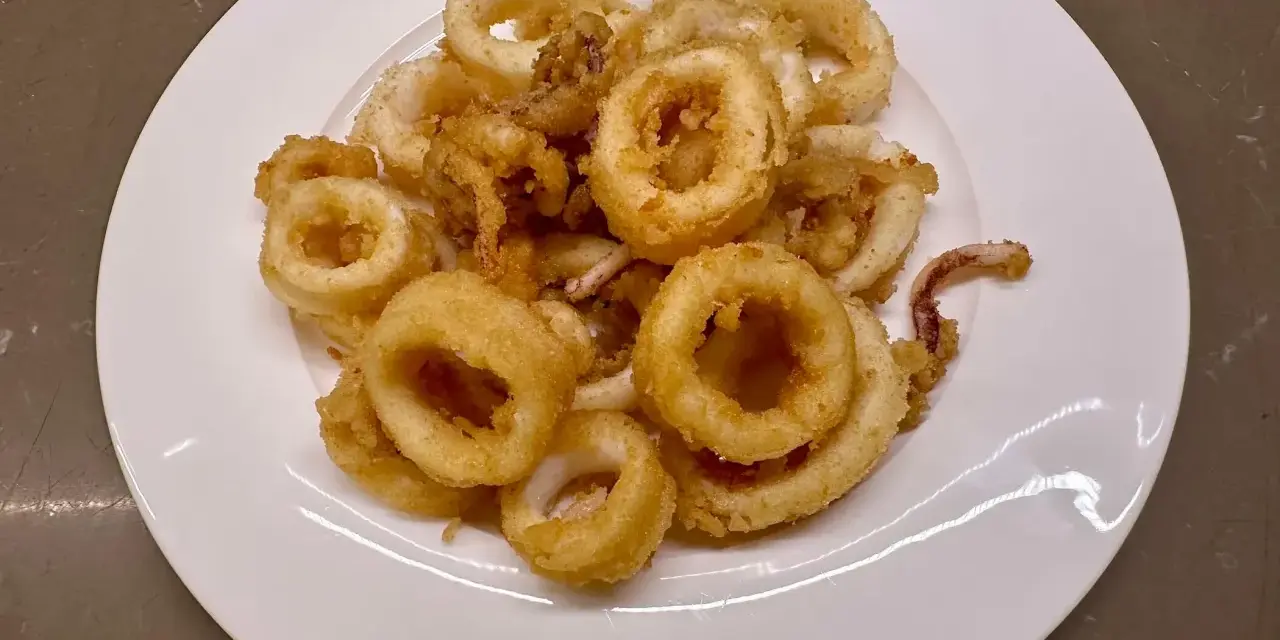 Un piatto bianco pieno di frittura di calamari dorata e croccante, un antipasto invitante.