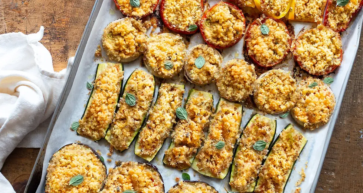 Verdure gratinate al forno: zucchine, melanzane, pomodori e peperoni ripieni di pangrattato e erbe aromatiche, cotti su una teglia.