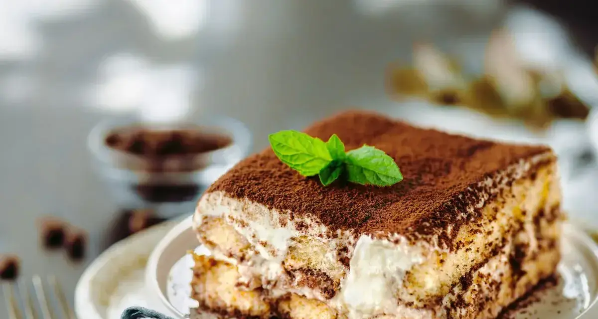Una fetta di tiramisù ricetta originale, cosparso di cacao e decorato con menta fresca.