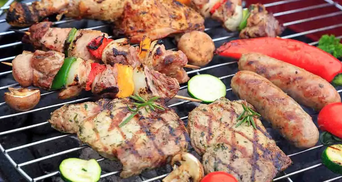 Grigliata di Ferragosto con spiedini, salsicce, bistecche, verdure e pomodori che cuociono sulla brace.
