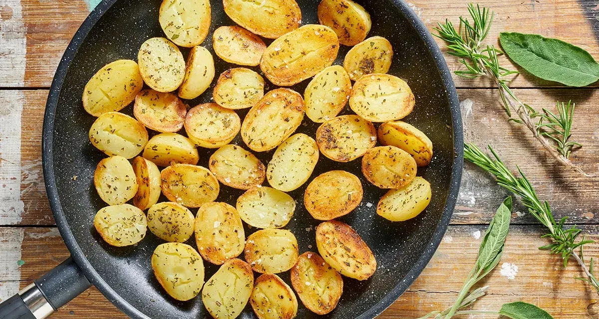 Patate novelle dorate e profumate in padella, condite con erbe aromatiche fresche, pronte per essere gustate.