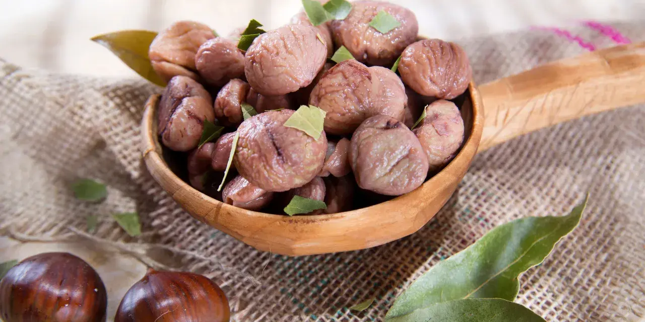 Un cucchiaio di legno trabocca di castagne bollite con buccia, guarnite con foglie verdi. Un assaggio autunnale.