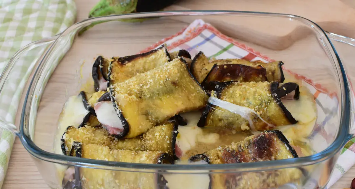 Involtini di melanzane alla siciliana appena sfornati, filanti e dorati, in una pirofila di vetro.