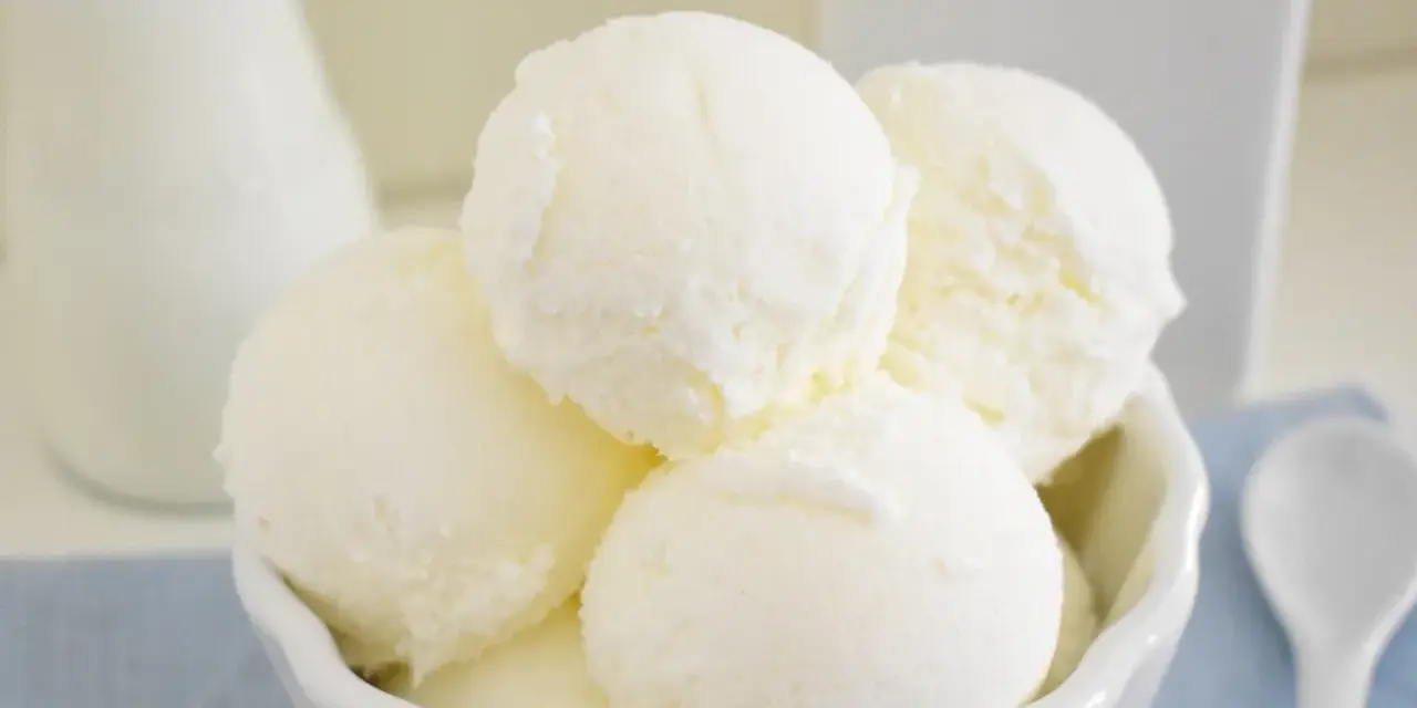 Coppa di gelato cremoso, risultato di una perfetta ricetta gelato con gelatiera. Latte fresco e cucchiaino bianco.