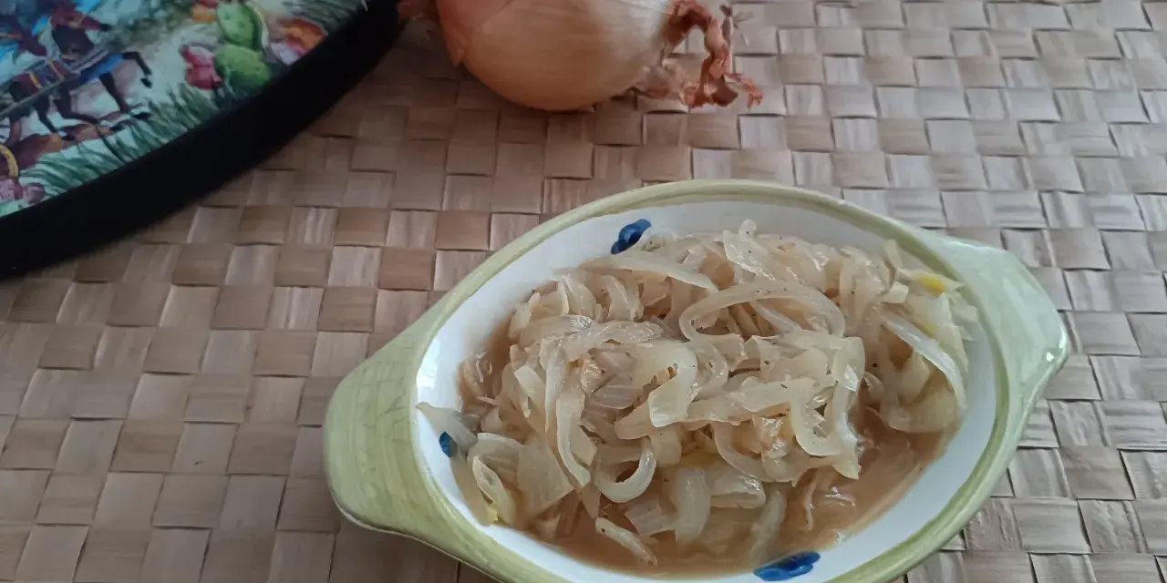 Ciotola con cipolle in agrodolce, accanto una cipolla intera e un piatto decorato.