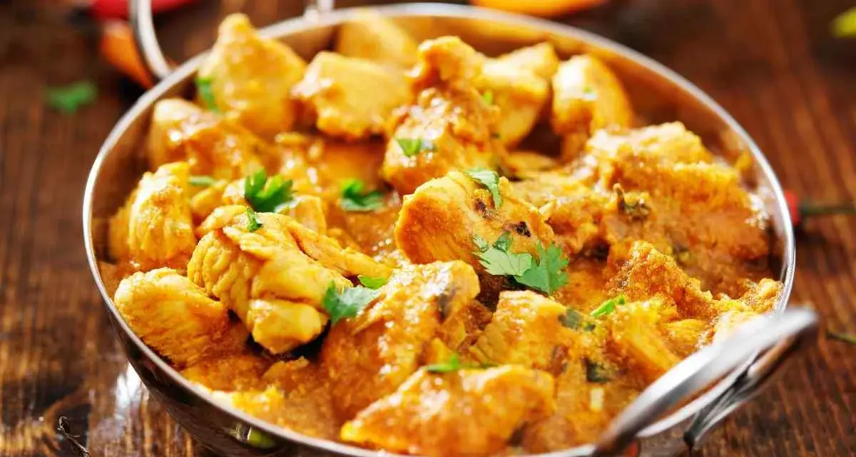Bocconcini di pollo al curry, un piatto speziato e profumato, servito in una ciotola metallica su un tavolo di legno.