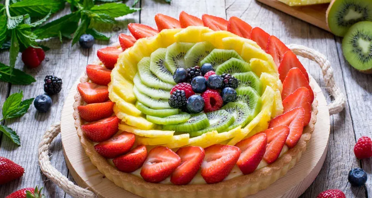 Una colorata crostata di frutta, con fragole, kiwi, ananas e frutti di bosco, su un tavolo di legno rustico.