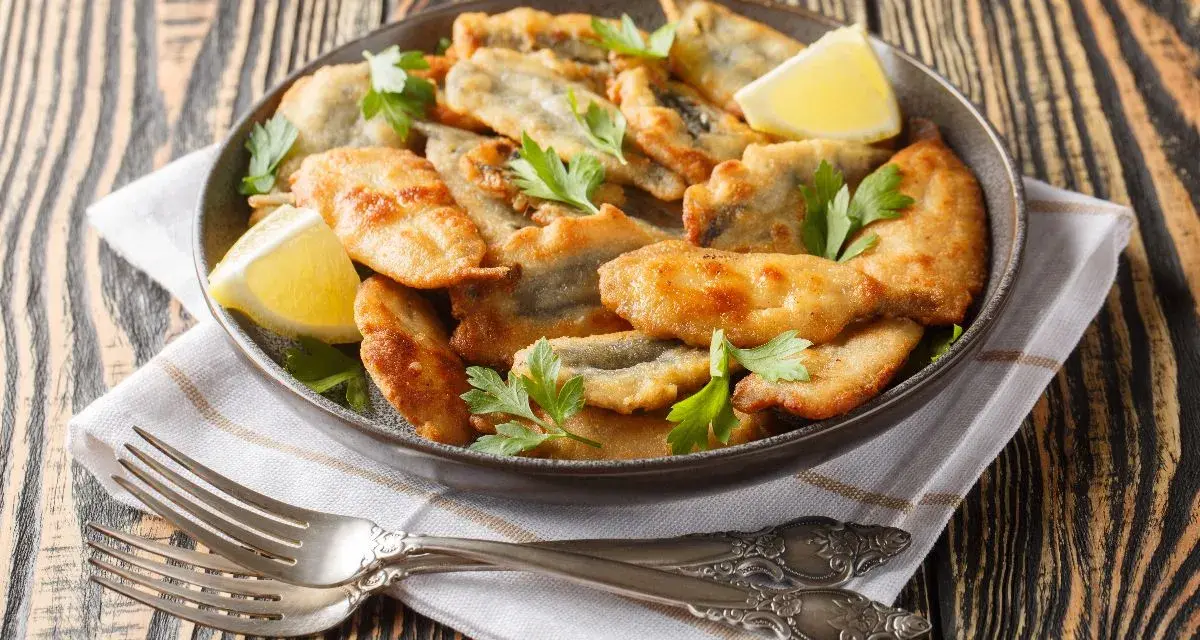 Piatto di acciughe ripiene alla ligure, dorate e croccanti, guarnite con prezzemolo fresco e spicchi di limone.