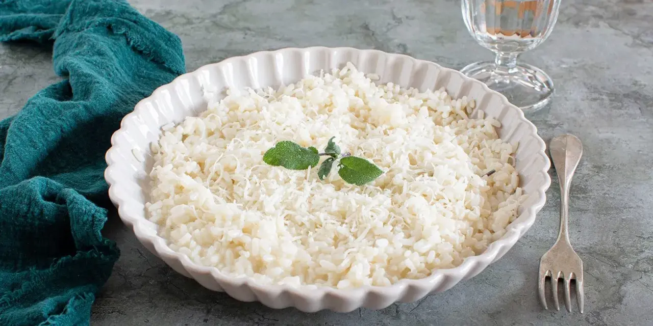 Piatto di riso in cagnone, cremoso e invitante, guarnito con foglie di salvia e parmigiano grattugiato.