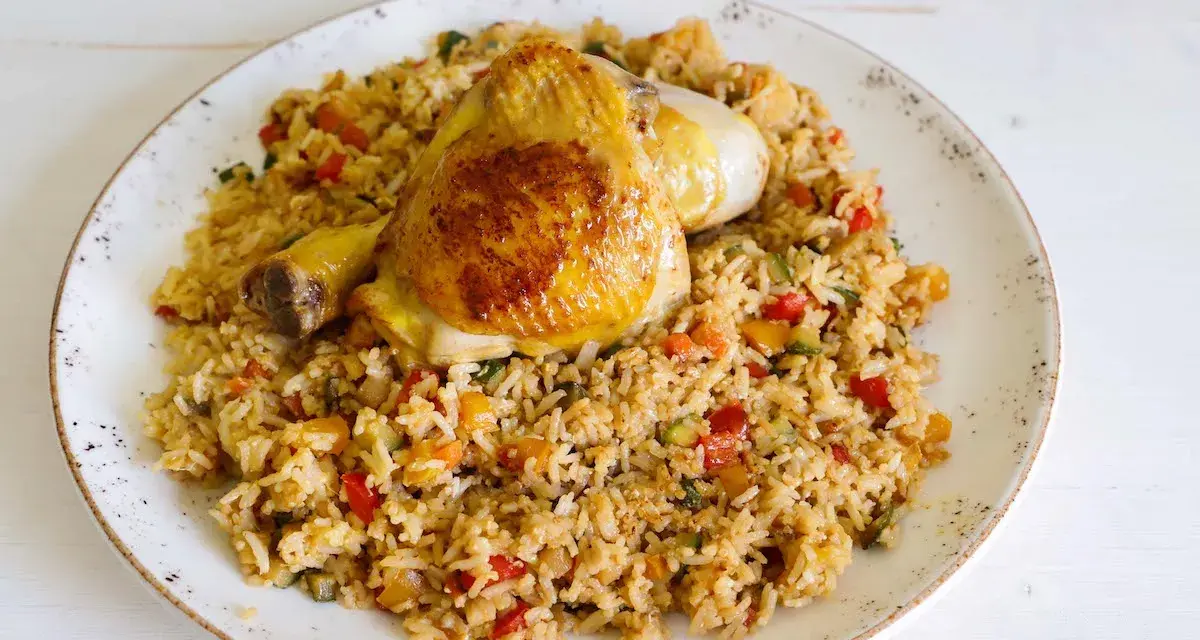 Fusi di pollo in padella serviti su un letto di riso saltato con verdure colorate.