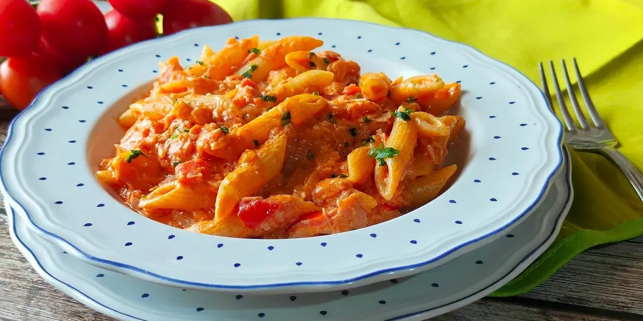 Piatto di penne al baffo cremose, con pomodorini freschi e prezzemolo tritato, servite su un piatto bianco con bordi blu.