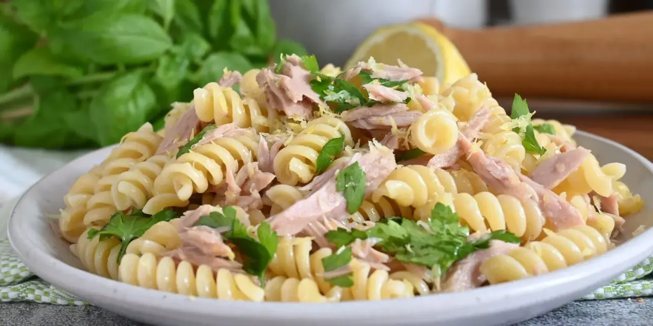Un piatto di pasta fredda tonno, con fusilli, tonno sfilacciato, prezzemolo fresco e scorza di limone. Perfetta per un pranzo estivo.