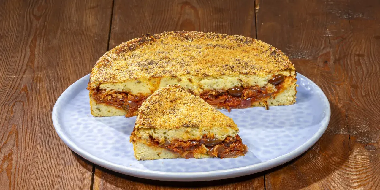 Pitta di patate ripiena di sugo, olive e cipolle, con una crosta dorata di pangrattato.