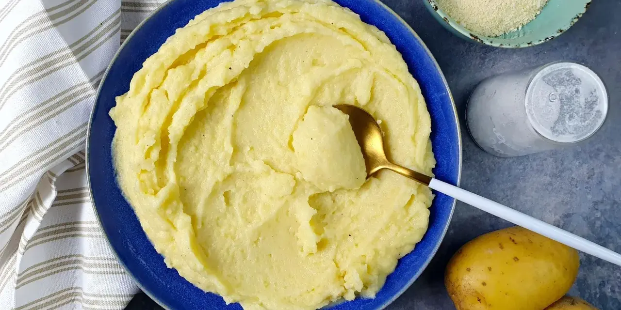 Un piatto invitante di puro di patate cremoso, pronto per essere gustato. Accanto, patate fresche, sale e formaggio grattugiato.