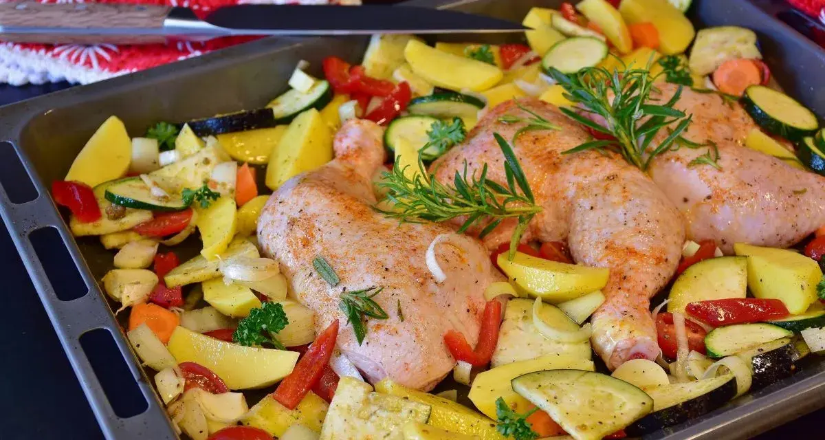 Sovracosce di pollo al forno con patate, zucchine, peperoni e rosmarino, pronte per essere infornate.