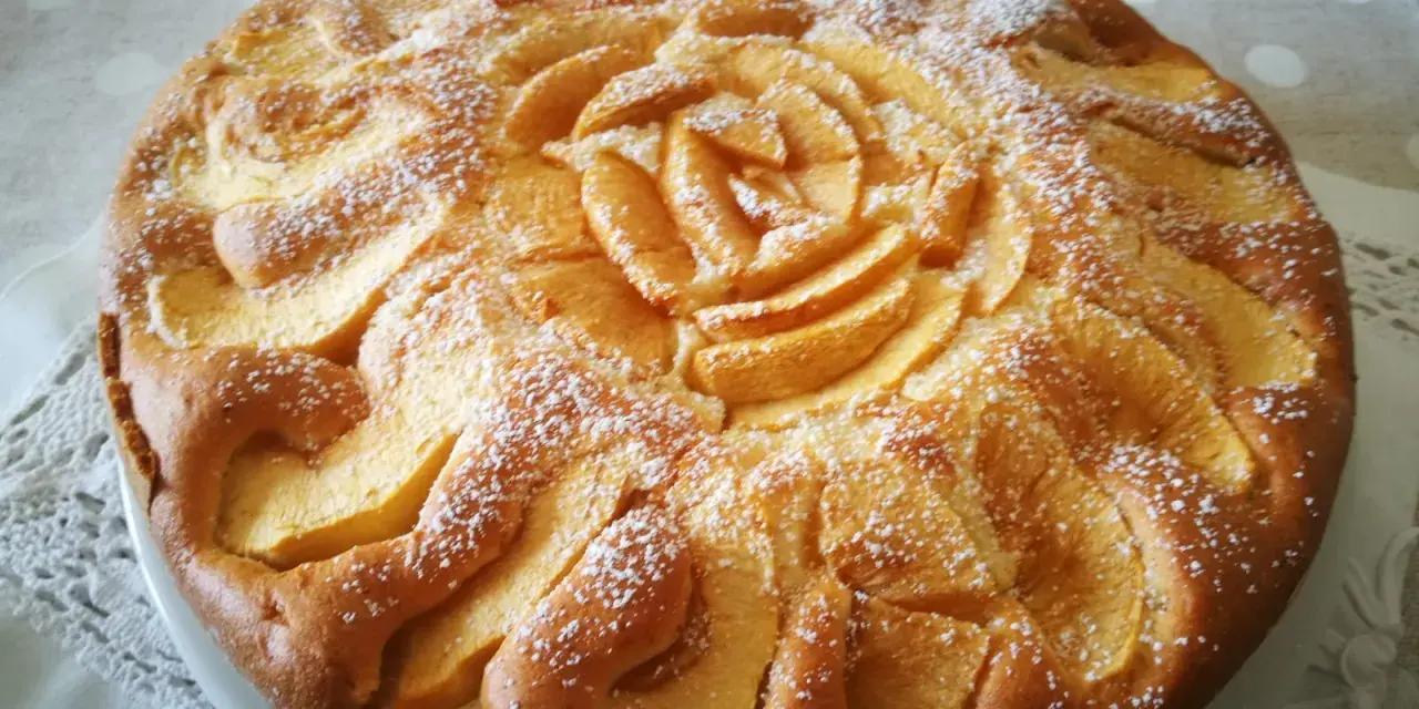 Deliziosa torta di mele senza glutine, con mele disposte a rosa al centro e spolverata di zucchero a velo.
