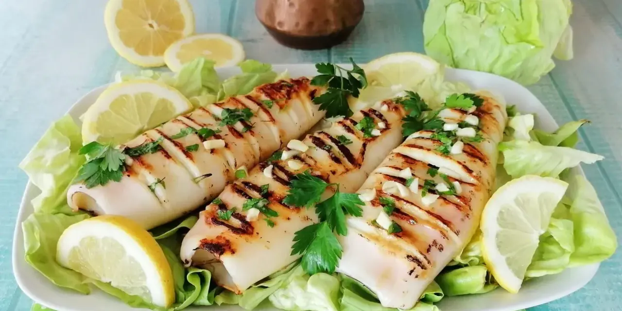 Tre calamari alla piastra succulenti, guarniti con aglio tritato, prezzemolo fresco e spicchi di limone, serviti su un letto di lattuga croccante.