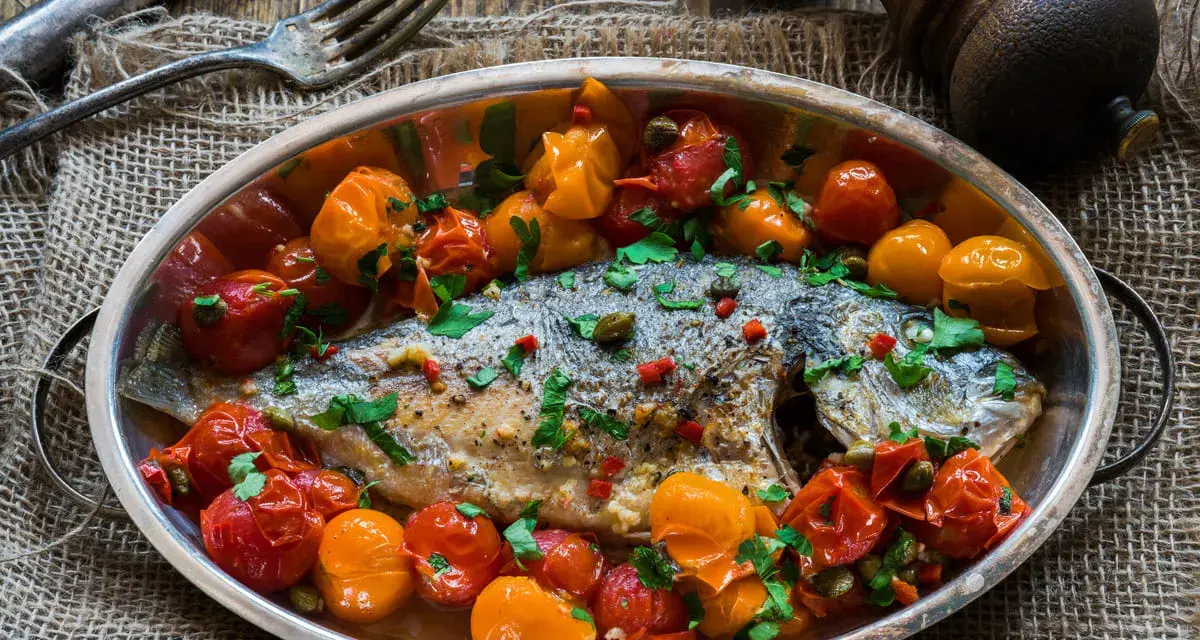 Orata all'acqua pazza, un piatto saporito con pomodorini, capperi e prezzemolo, pronto per essere gustato.