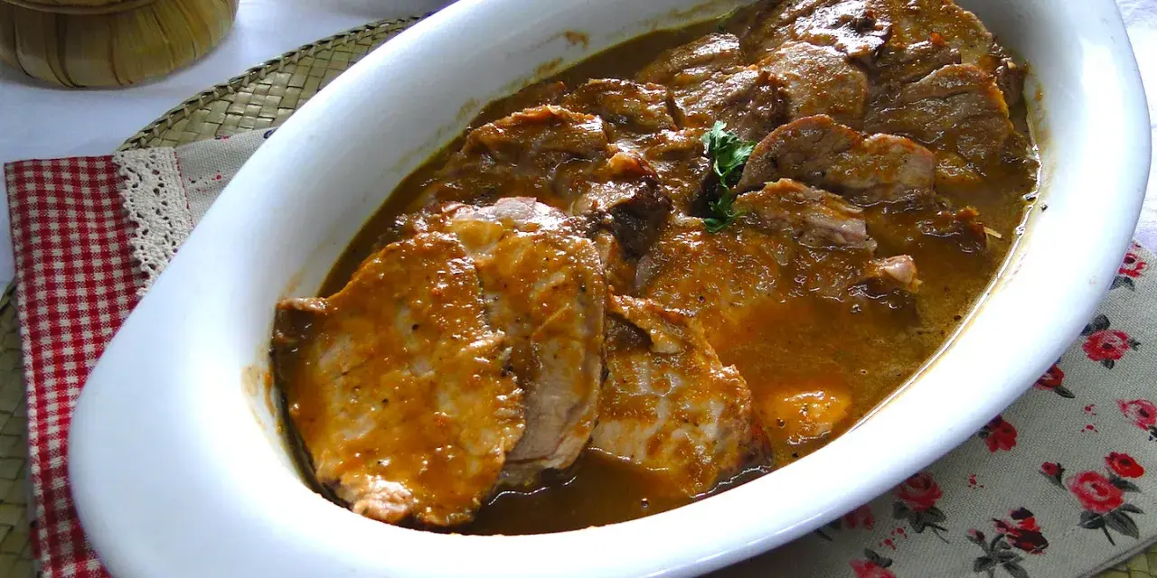 Succulento arrosto di maiale in salsa, servito in una pirofila bianca, pronto per essere gustato.