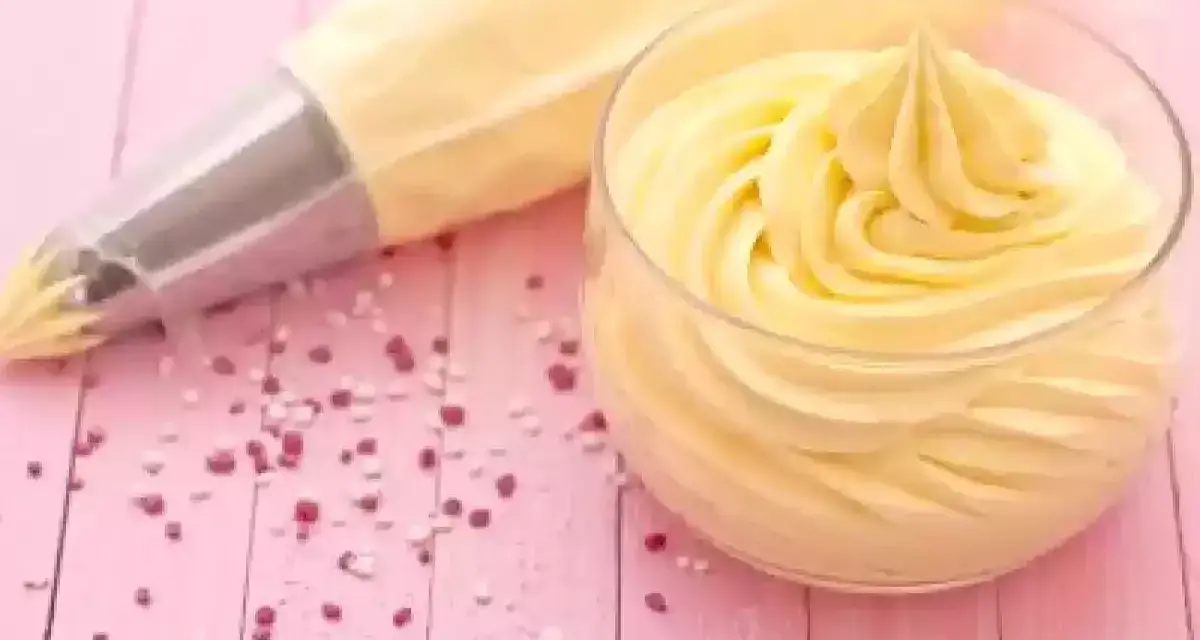 Sac à poche con crema al burro pronta per decorare, accanto a un bicchiere colmo della stessa soffice crema.