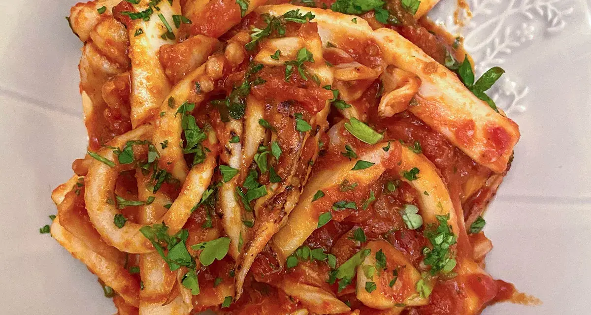 Un piatto invitante di calamari in umido, conditi con una ricca salsa al pomodoro e prezzemolo fresco tritato.