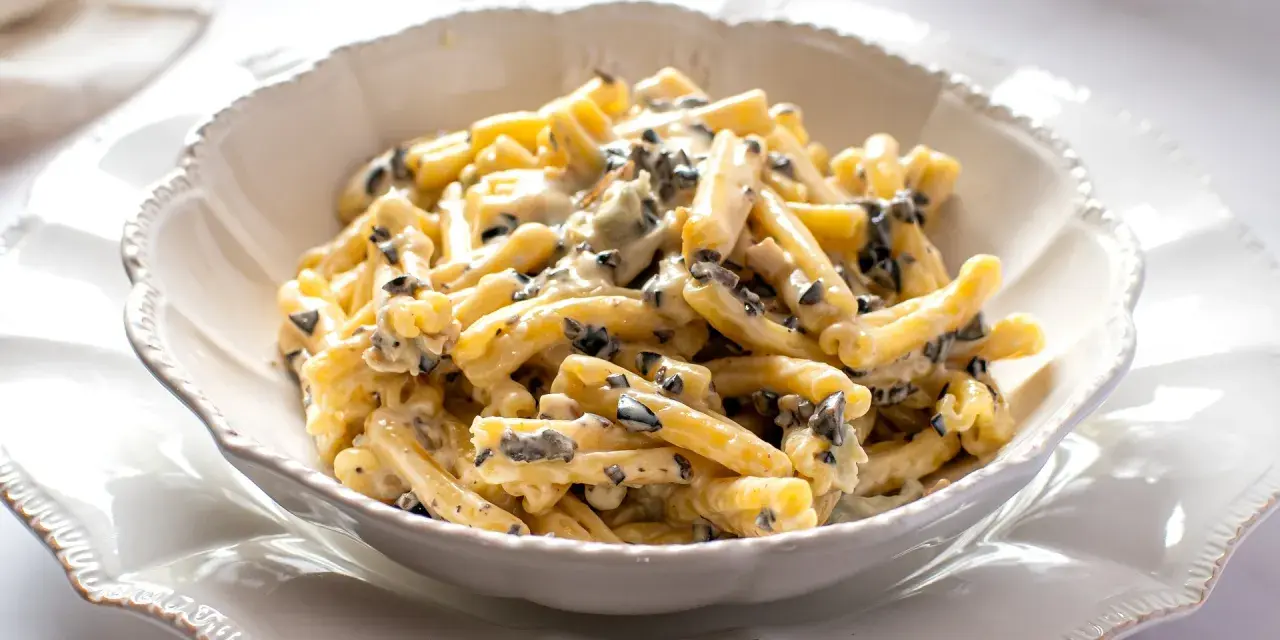Un piatto di pasta alla cenere cremosa, con pezzetti scuri di olive, servita in una ciotola bianca decorata.