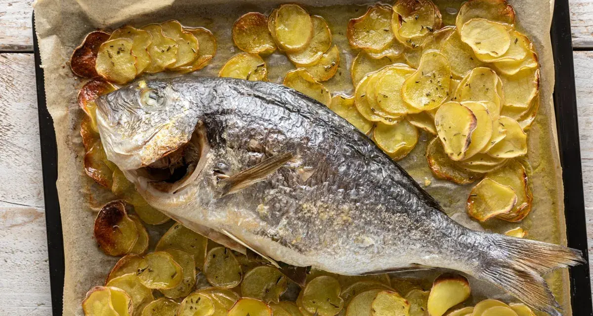 Orata al forno dorata e succulenta, adagiata su un letto di patate croccanti e aromatiche.
