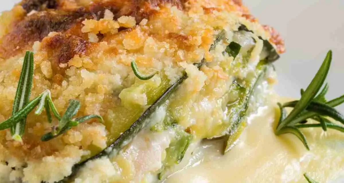 Una fetta di parmigiana di zucchine bianca senza besciamella, dorata e croccante, con rosmarino fresco.