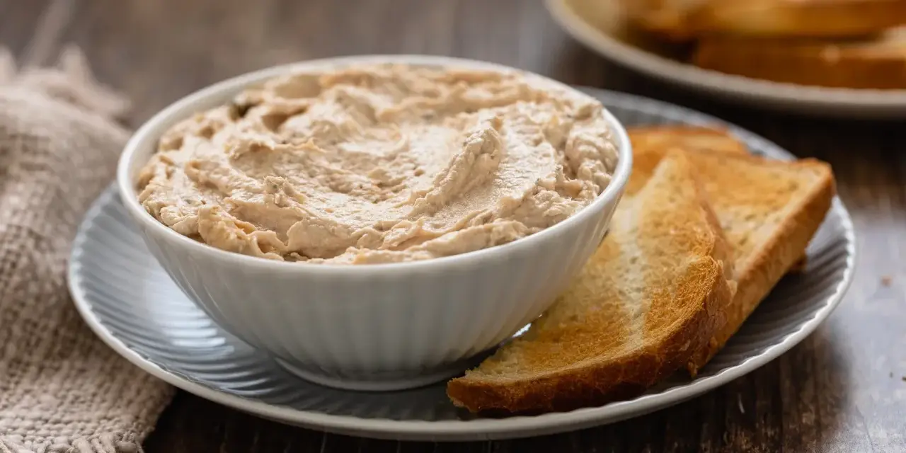 Una ciotola di cremosa mousse di tonno, servita con fette di pane tostato dorato. Perfetta per un aperitivo veloce.