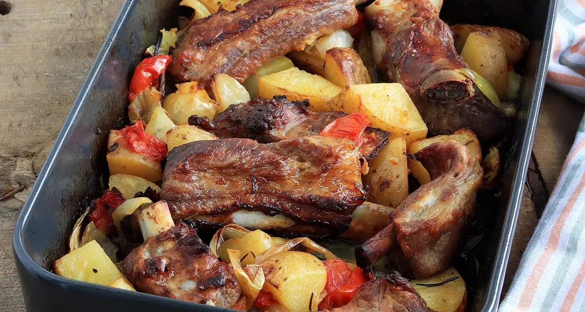 Succulente costine al forno con patate, peperoni e cipolle in una teglia.