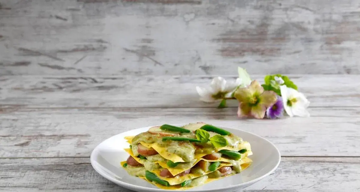 Lasagne al pesto con fagiolini e patate, un piatto colorato e gustoso su un tavolo di legno.