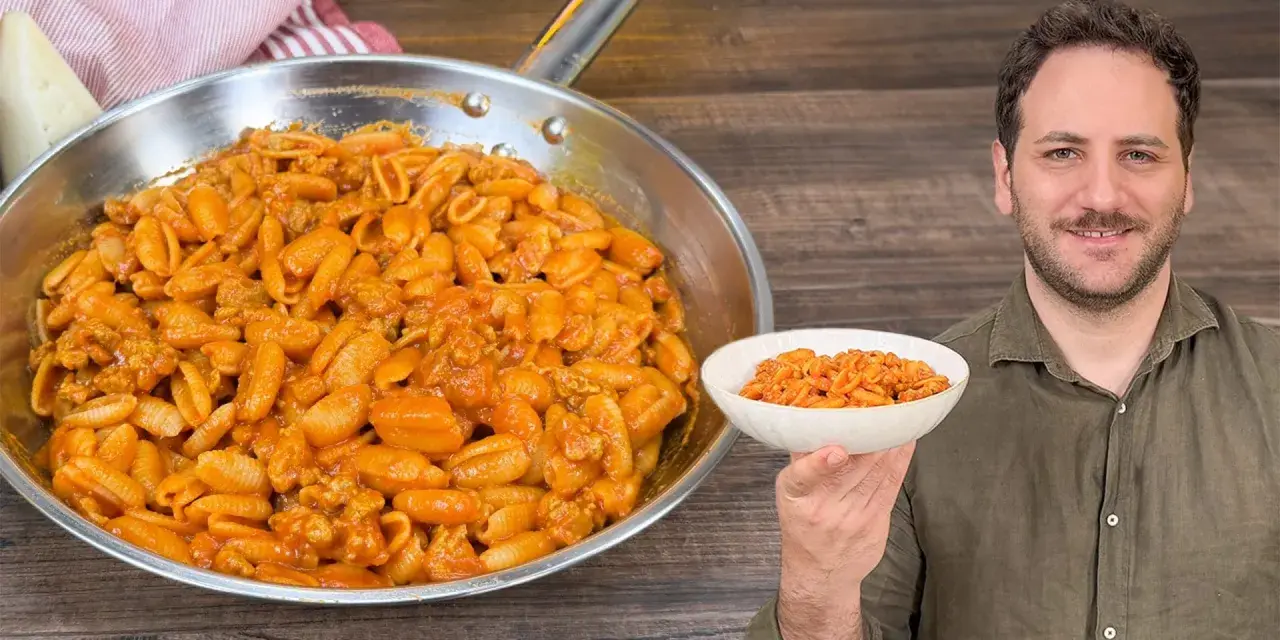 Un uomo sorride mostrando una ciotola di gnocchetti alla campidanese, accanto a una padella piena dello stesso piatto.