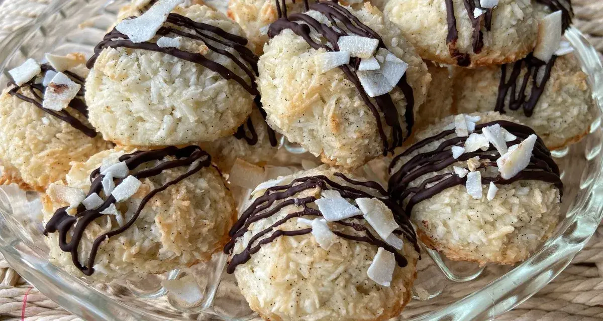 Deliziosi dolcetti al cocco, ricoperti da cioccolato fondente e scaglie di cocco croccante, su un piatto di vetro.
