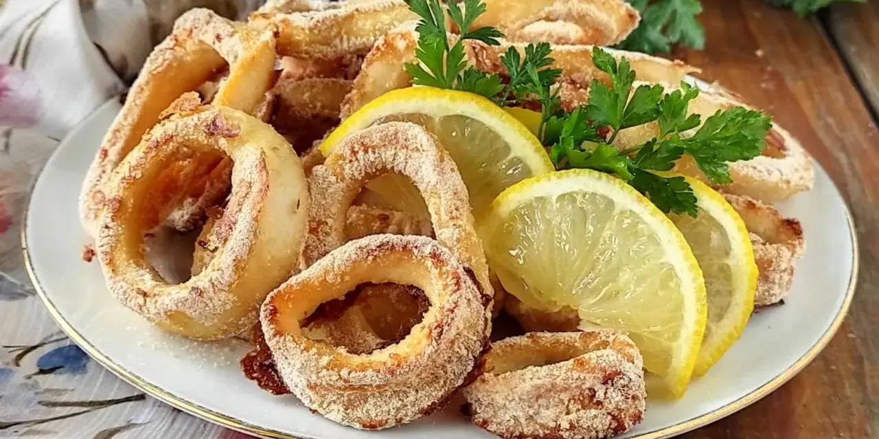 Anelli di calamari al forno dorati e croccanti, guarniti con spicchi di limone fresco e prezzemolo.