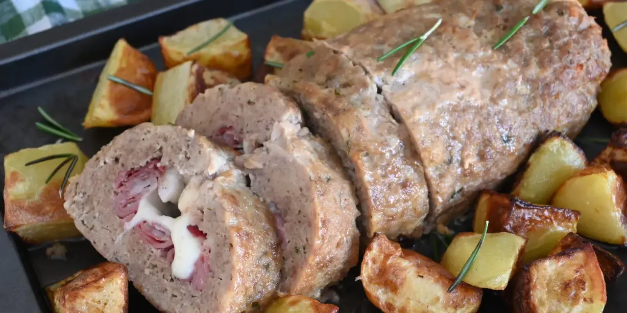 Polpettone al forno ripieno di prosciutto e formaggio filante, servito con patate arrosto e rosmarino.