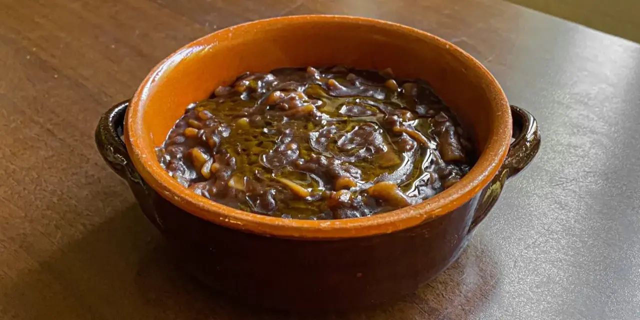 Un gustoso piatto di pasta e lenticchie, condito con olio d'oliva, servito in una ciotola di terracotta su un tavolo di legno.